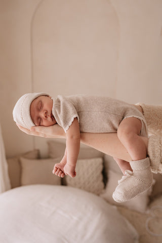 Sleeping baby in mothers arms wearing neutral knitted romper, hat, and booties