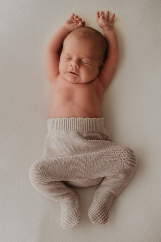 Stretching baby wearing grey knitted trousers 
