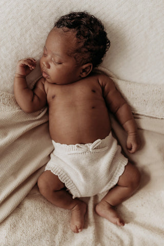 Sleeping newborn baby lying on beige blanket wearing knitted bow bloomers