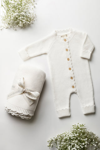White baby blanket tied with an Isls & Fraser ribbon, and white knitted baby romper