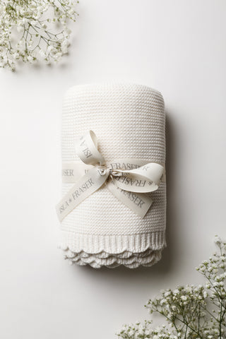 White knitted baby blanket on white background tied with an Isla & Fraser ribbon