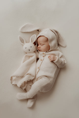 Baby wearing a cream hooded bunny outfit cuddling a matching bunny comforter