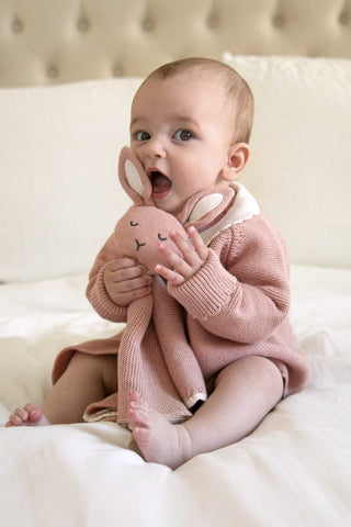 Baby sitting up cuddling a pink bunny comforter