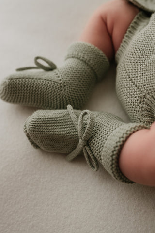 Baby wearing sage green knitted bow booties
