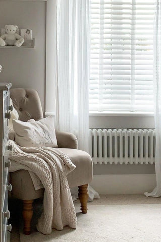 Neutral nursery with sheer drapes, a chair with a cushion and blanket