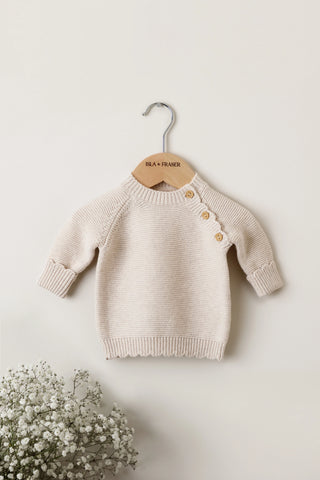 Beige knitted baby jumper with buttons on an Isla & Fraser wooden hanger