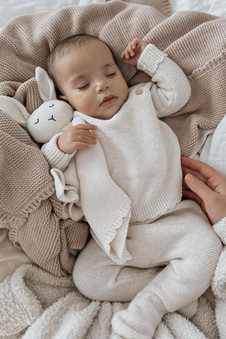 Sleeping Baby lying on blankets, wearing a knitted outfit, cuddling a bunny comforter