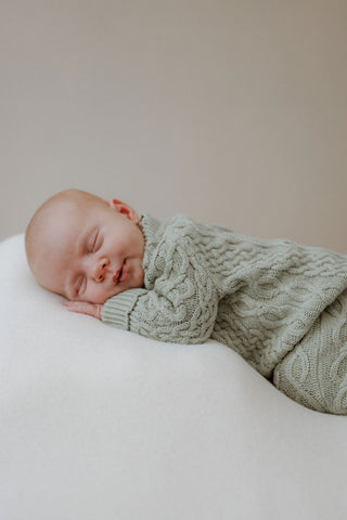 Sleeping newborn baby smiling wearing a sage green cable knit baby romper