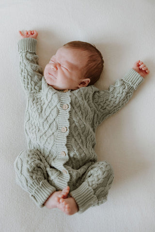 Newborn baby stretching wearing a sage green cable knit romper