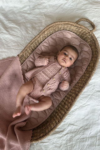Baby in basket wearing pink knitted outfit with pink blanket
