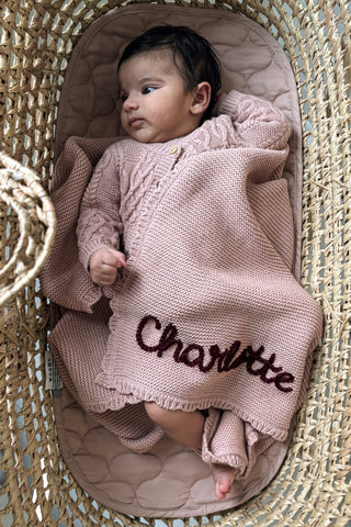 Baby in moses basket wearing pink knitwear with a 'Charlotte' embroidered name blanket