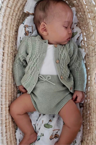 Sleeping baby in moses basket with sage green knitted outfit