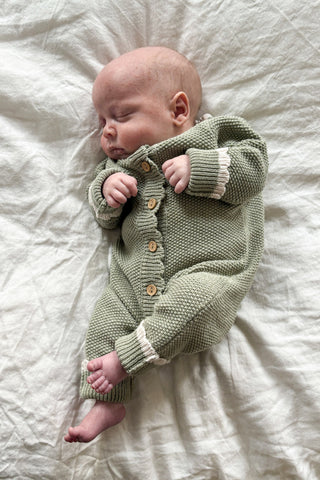sleeping baby on linen sheet wearing knitted sage green baby romper