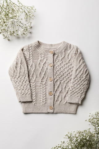 Neutral beige cable knit baby cardigan on a white backdrop with flowers