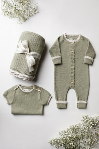 Sage green knitted baby blanket tied with an Isla & Frase ribbon, romper, and folded bodysuit