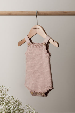 Knitted Pink Baby Romper on a wooden rail on a wooden Isla & Fraser hanger with flowers